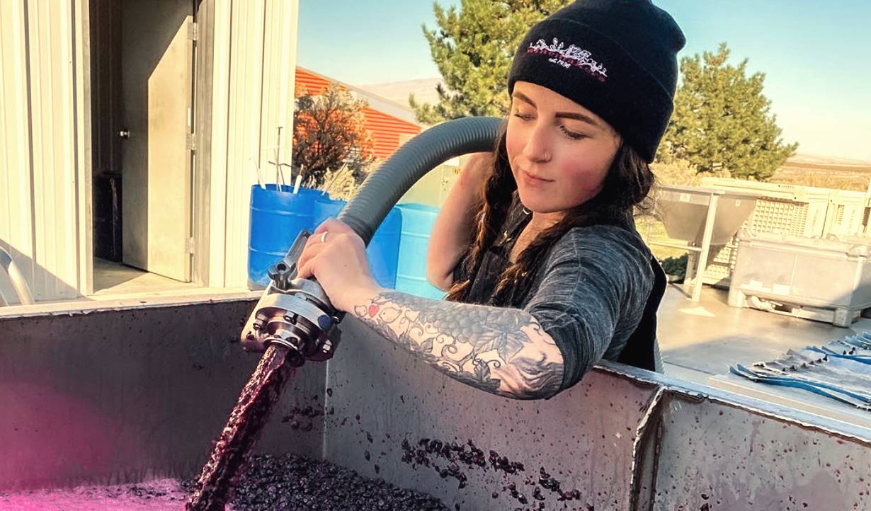 Young female winemaker pumping over a vat of crushed red grapes