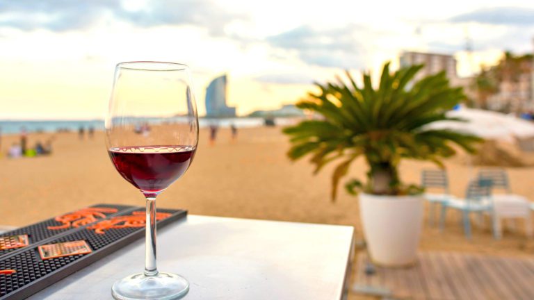 A glass of red wine on a bar overlooking the beach in Barcelona in Spain, at sunset