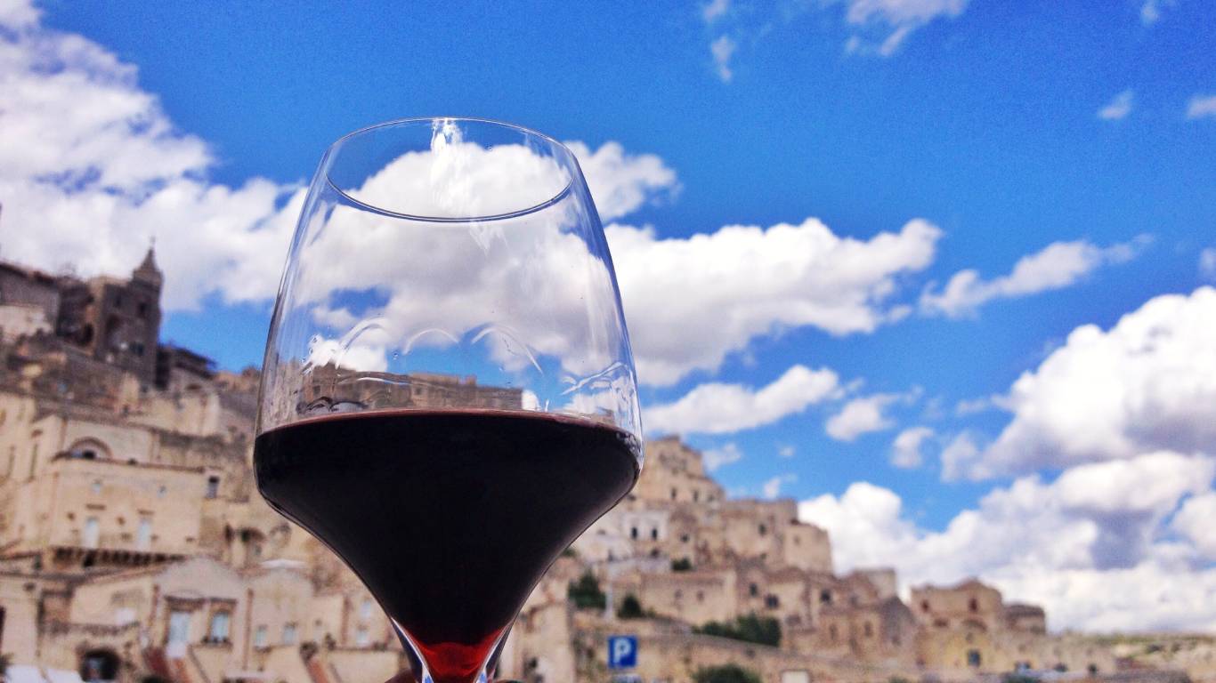 Glass of red wine being held up with ancient town of Matera, Basilicata in the background