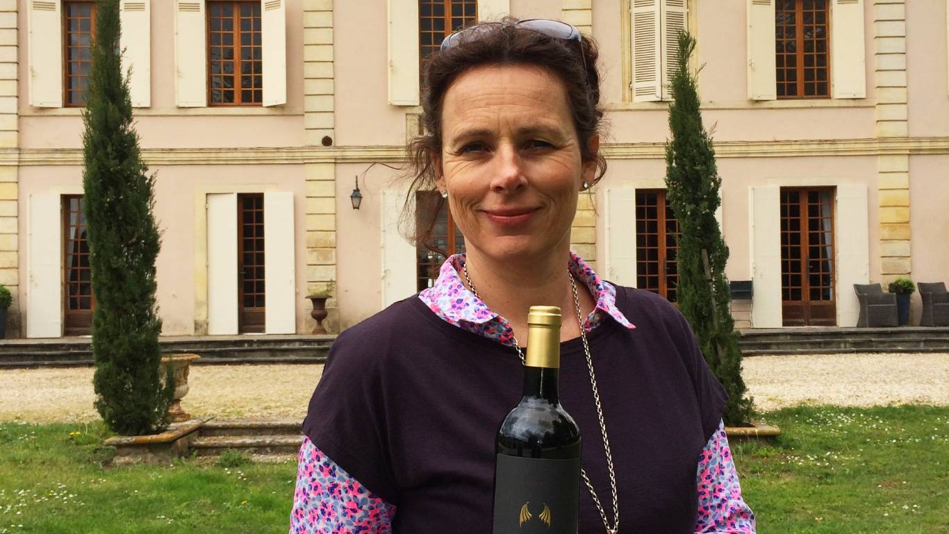 One of our women in wine, Nicola Allison of Château du Seuil, holding a bottle of red wine and standing in front of her château