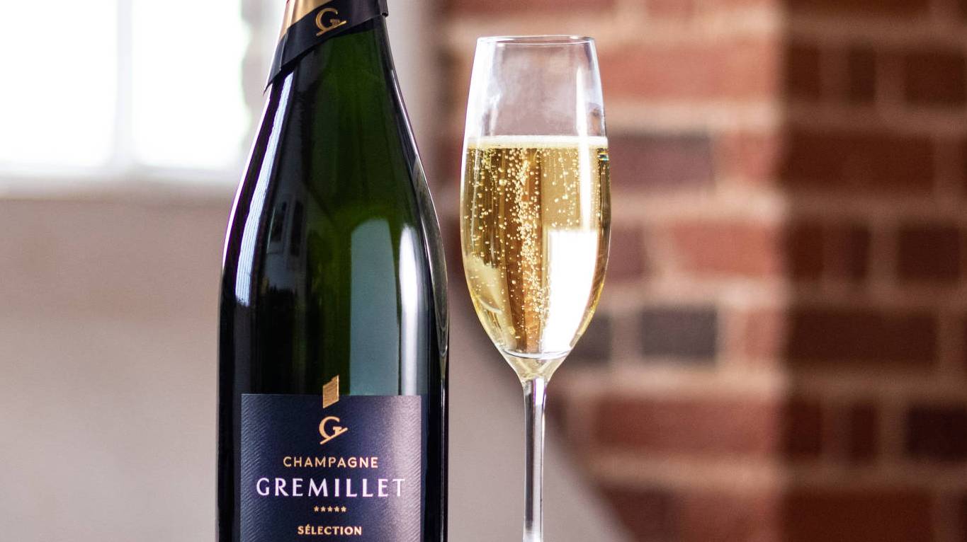 A glass of Champagne next to a bottle of Champagne in front of a window and brick wall