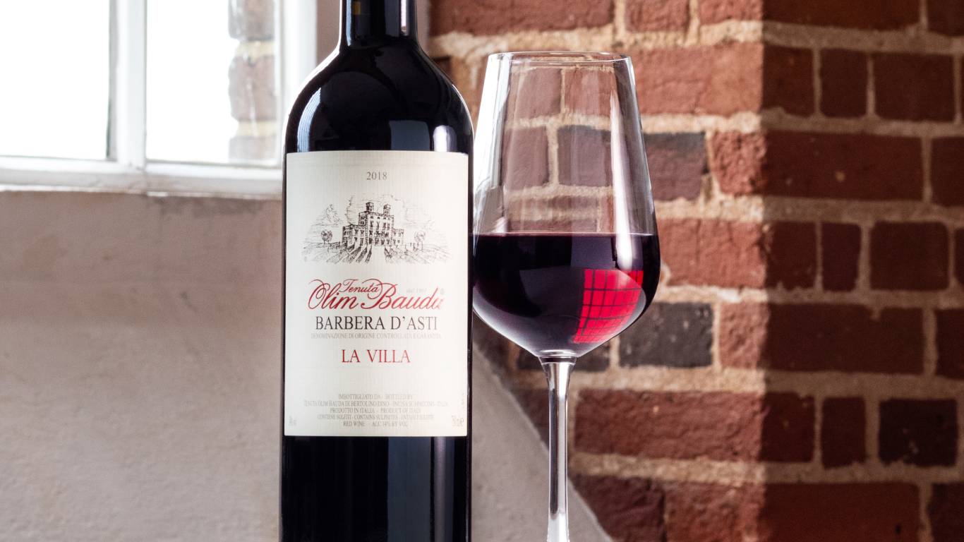 A glass of red wine next to a bottle of red wine in front of a window and brick wall