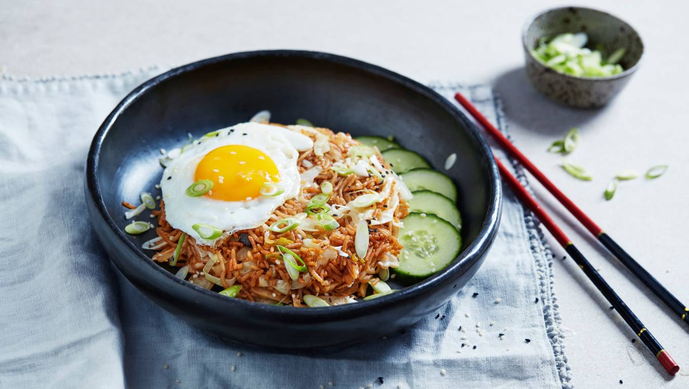 Korean fried rice dish topped with a fried egg in a black bowl sat on a table with chopsticks