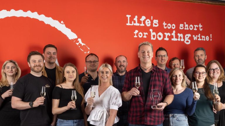 Virgin Wines staff holding glasses of sparkling wine in front of a red wall, with Virgin Wines CEO Jay Wright holding the Specialist Online Drinks Retailer of the Year award