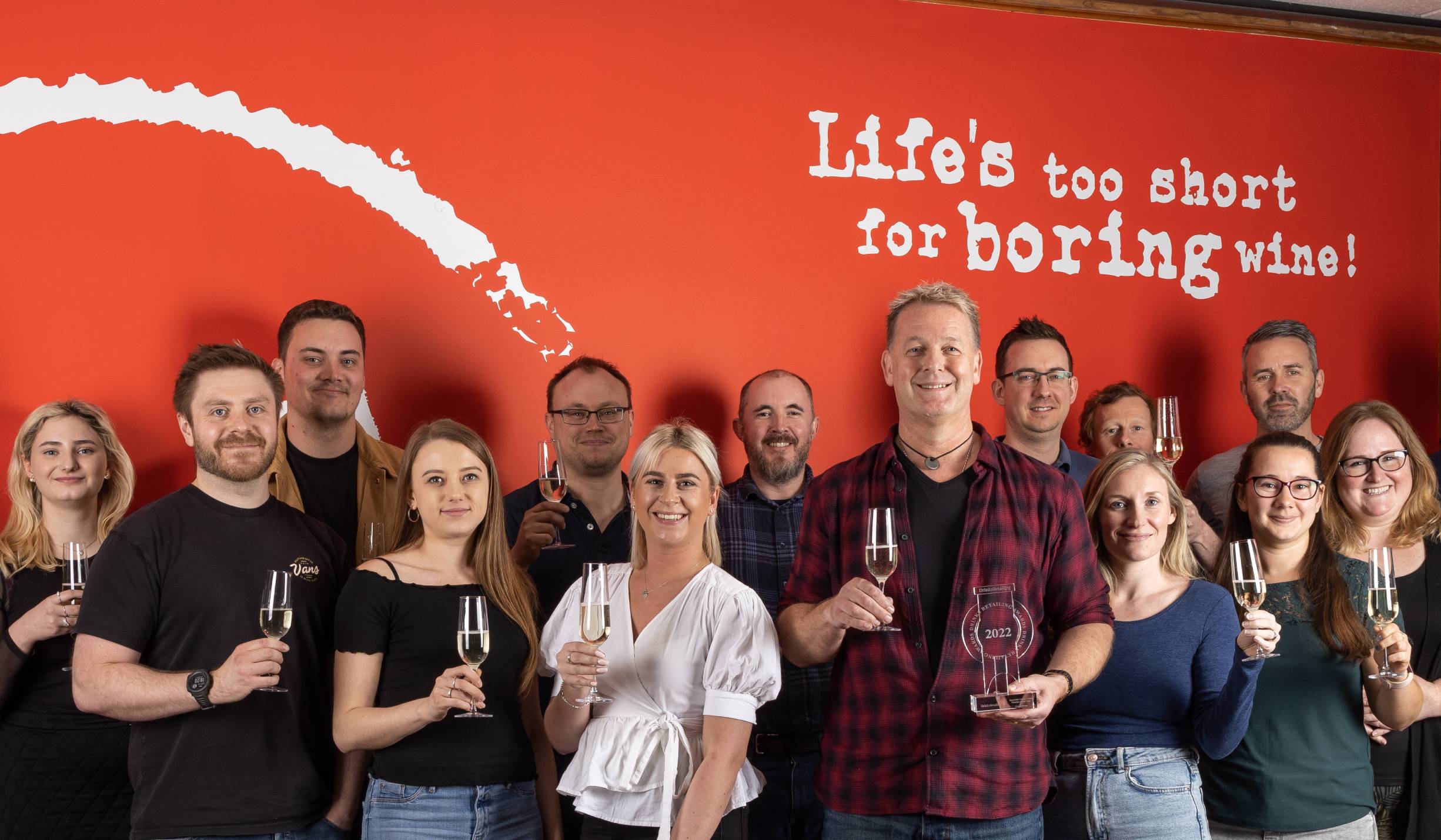 Virgin Wines staff holding glasses of sparkling wine in front of a red wall, with Virgin Wines CEO Jay Wright holding the Specialist Online Drinks Retailer of the Year award