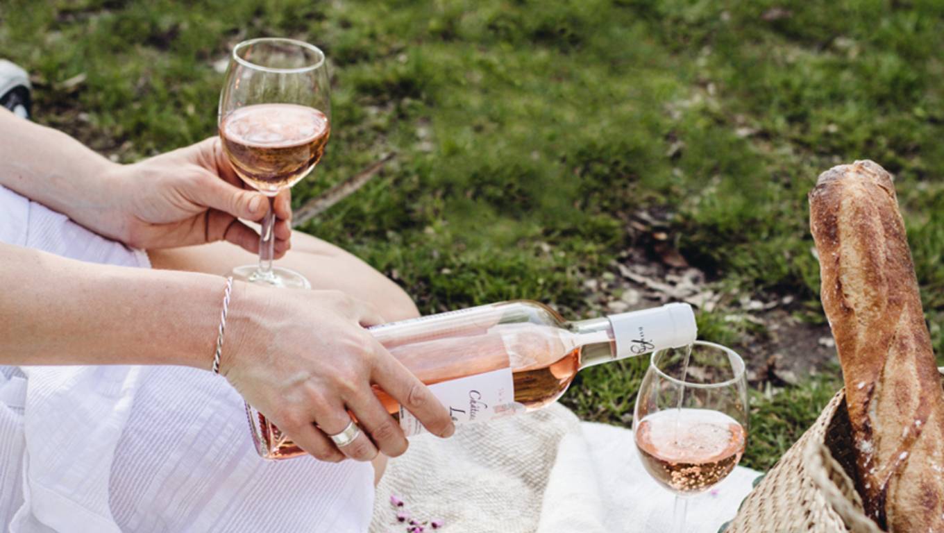 hand pouring a glass of rosé on a picnic blanket