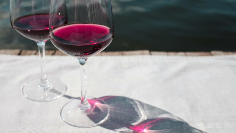 Two glasses of light-bodied red wine on a white table cloth outdoors by a lake in the sunshine