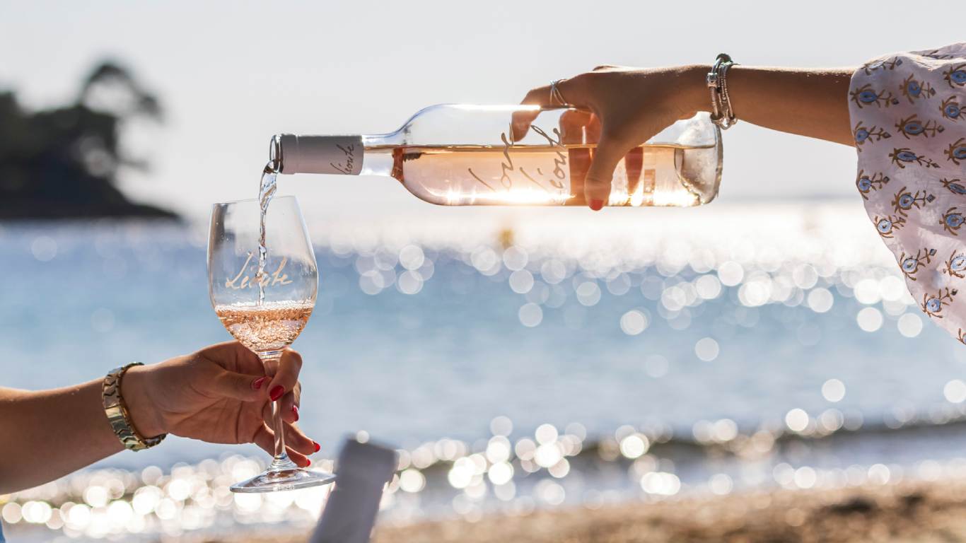 Woman pouring Provence rose into a wine glass on a beach in front of the sea