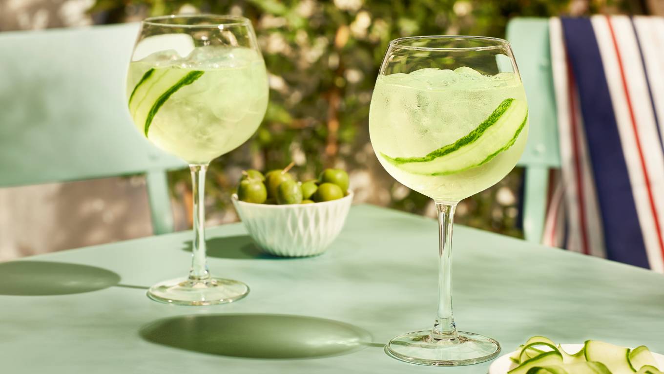 Two sauvignon blanc cocktails on table in garden garnished with cucumber next to bowl of olives