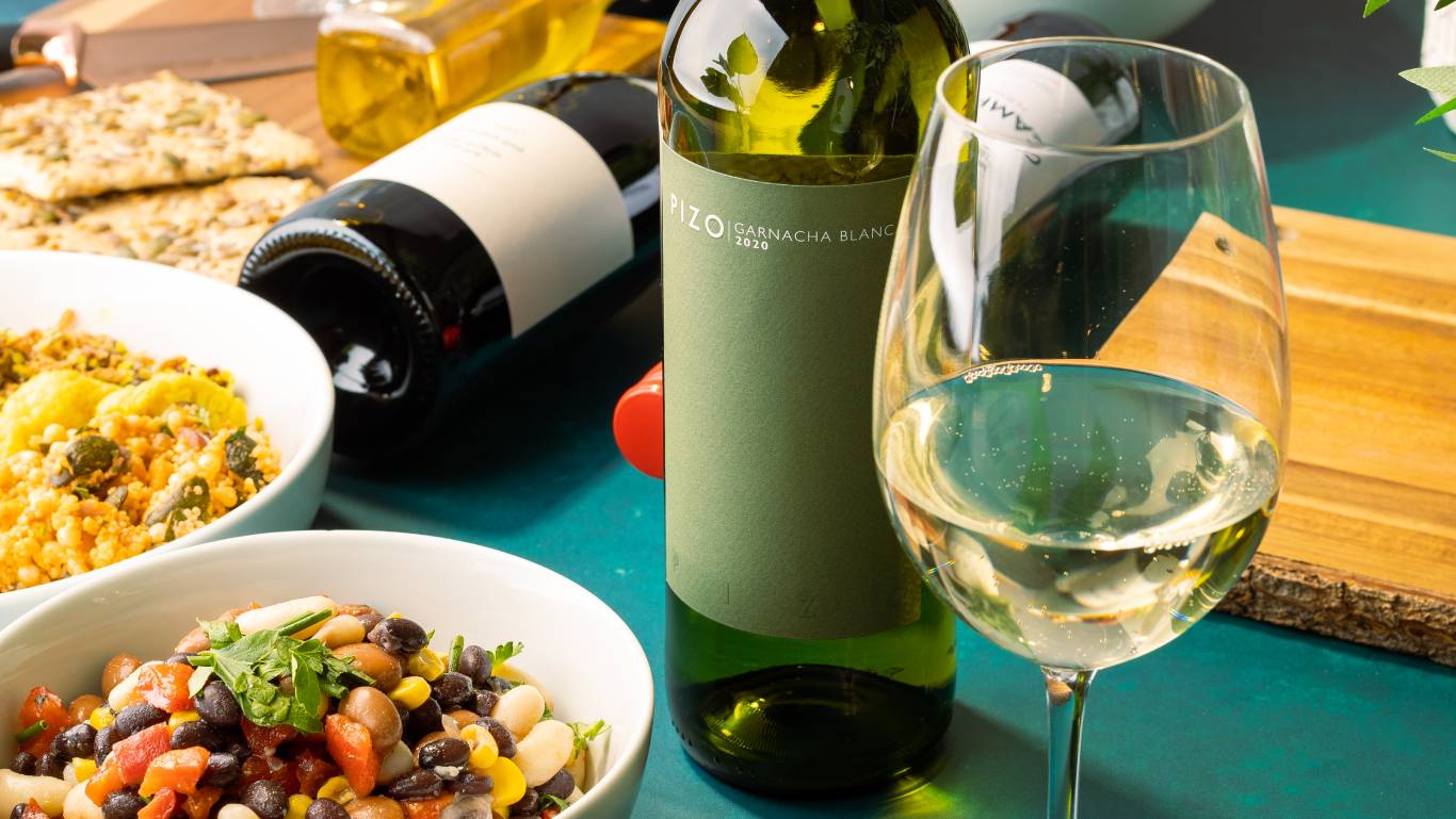 Bottle of vegan white wine on a table with plates of vegan food and other bottles of vegan wine