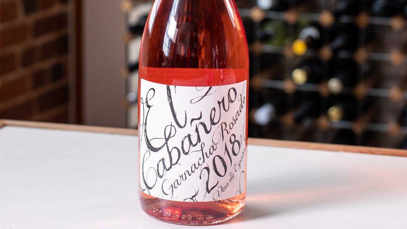 Bottle of Garnacha Rosado on a white table in front of a wine rack