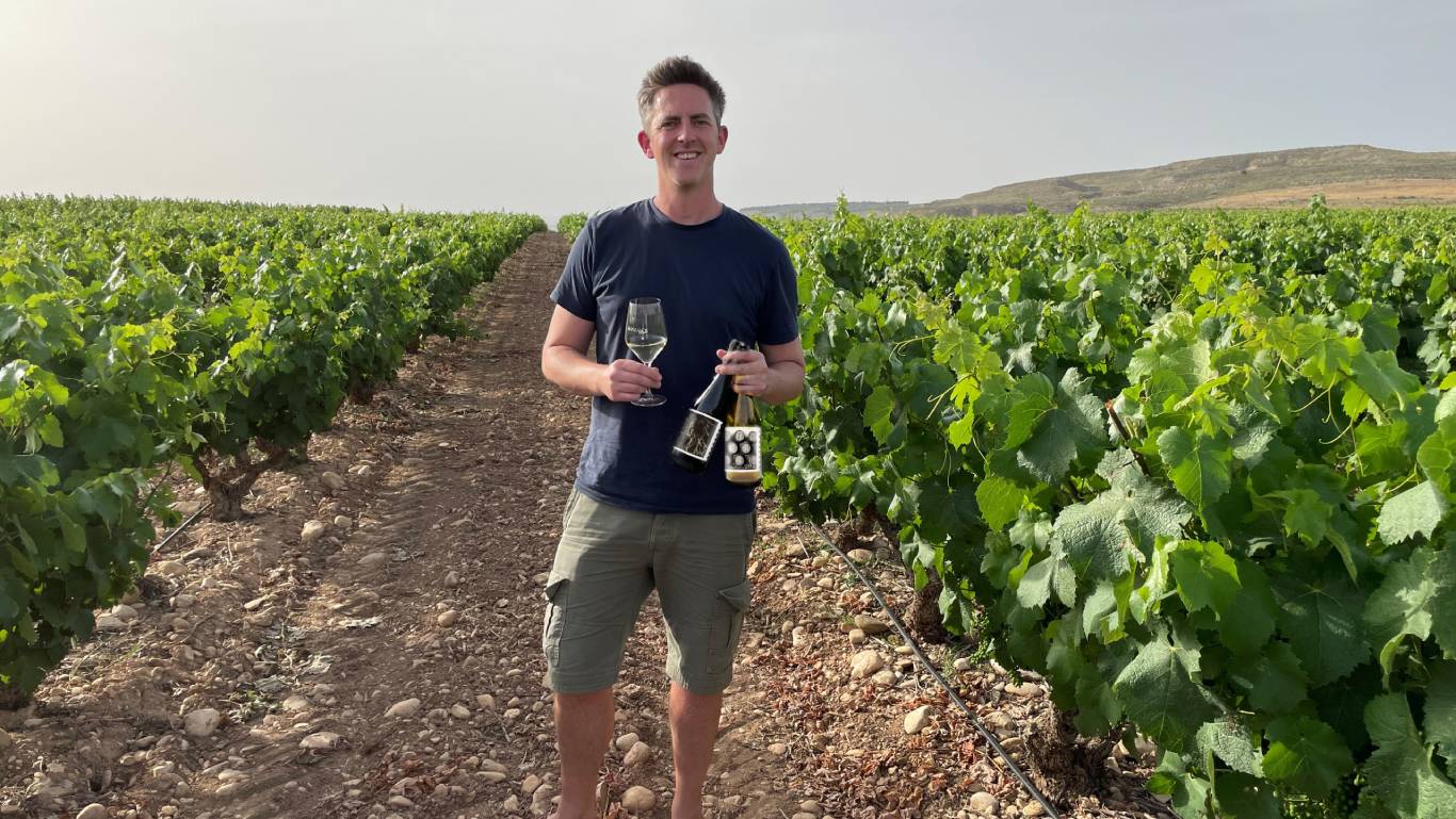 Alex, Wine Buyer at Virgin Wines, stood in a vineyard in Rioja holding two bottles of wine he blended in Rioja