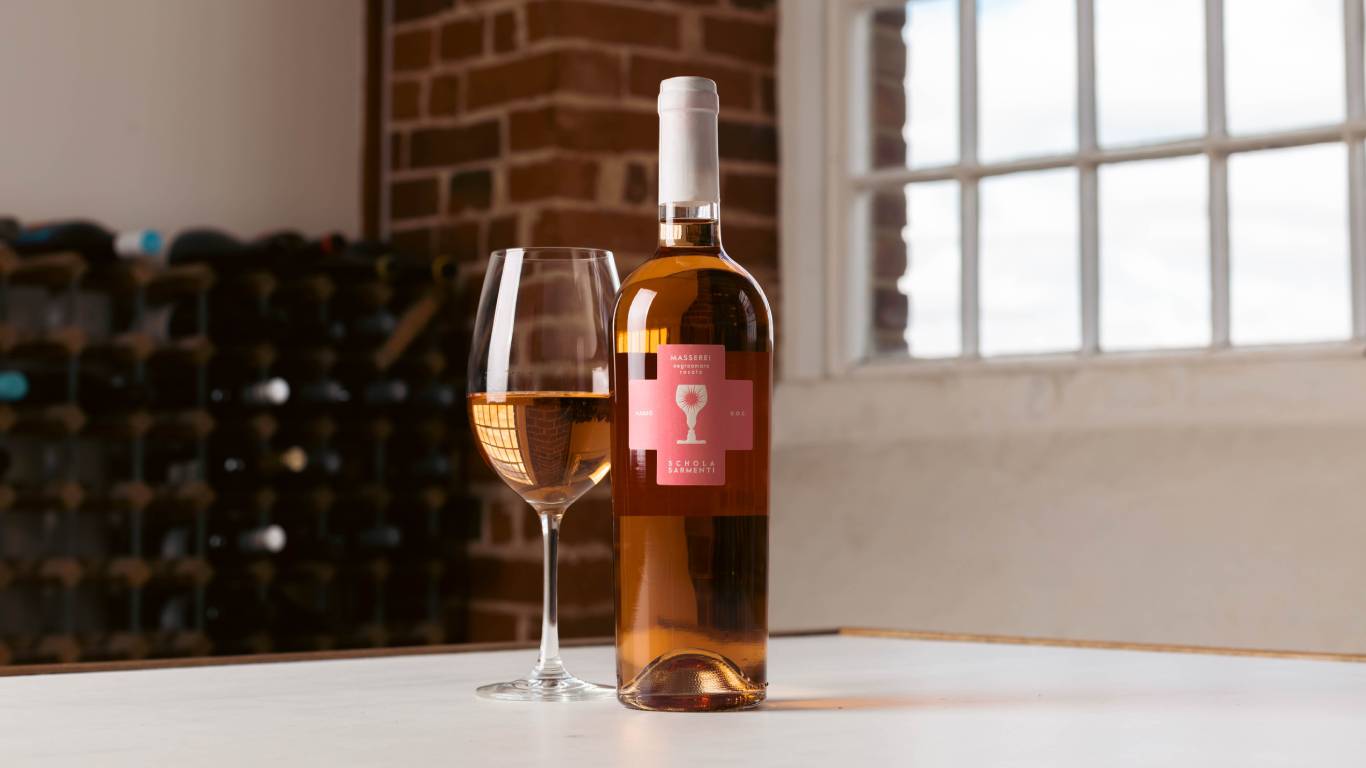 Bottle of Rosato next to a glass of Rosato on a table in front of a window
