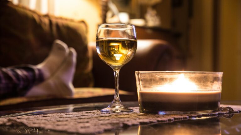 Glass of white wine on table in cosy living room next to candale