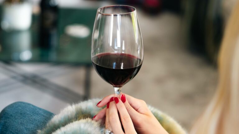 Woman holding a glass of modern Bordeaux red wine on a sofa by a coffee table
