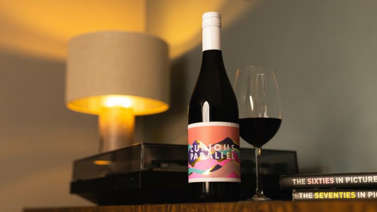 Bottle of Curious Parallel, a red wine made in Romania, by a record player in a cosy living room