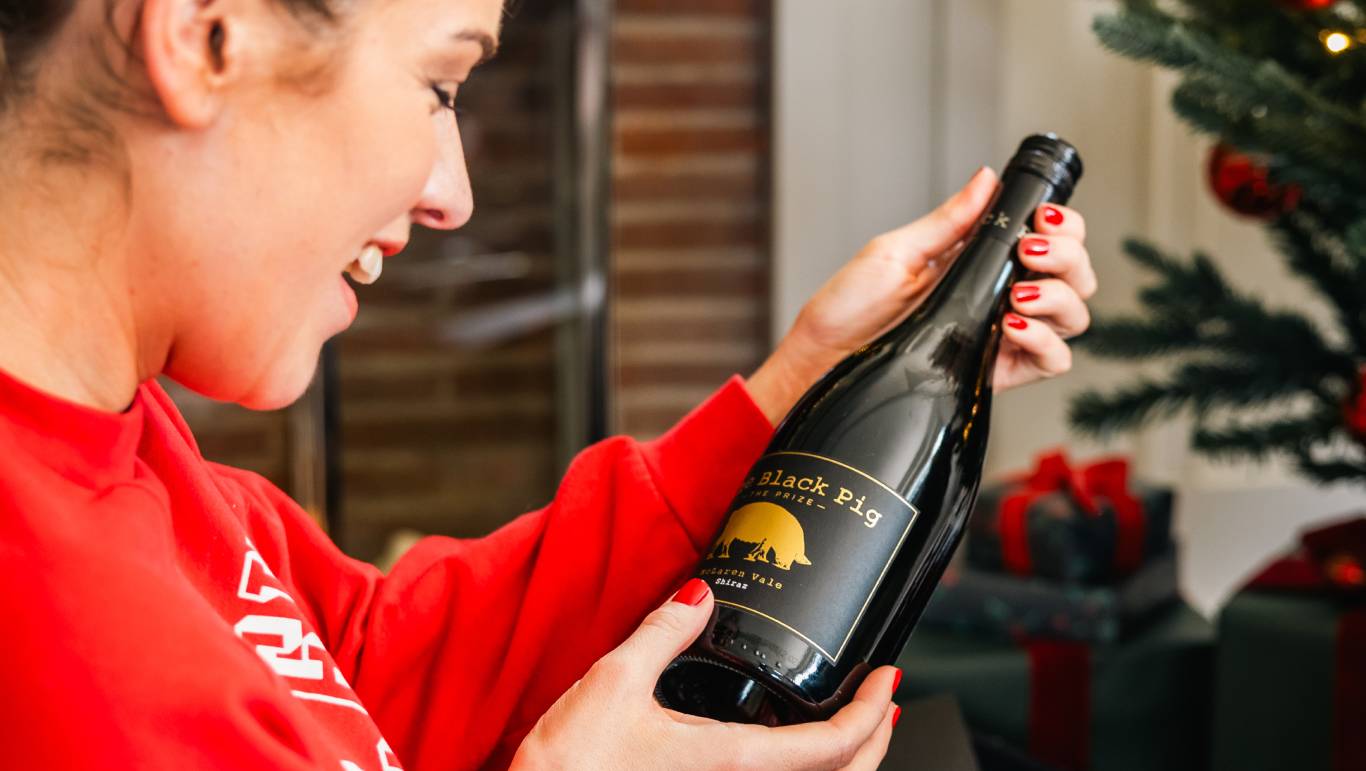 Happy woman sat by a Christmas tree opening a wine gift from Virgin Wines