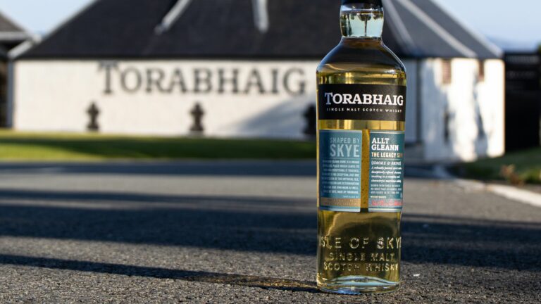 Bottle of Torabhaig whisky with the distillery in the background