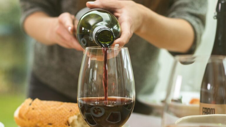 Woman pouring red wine into a red wine glass