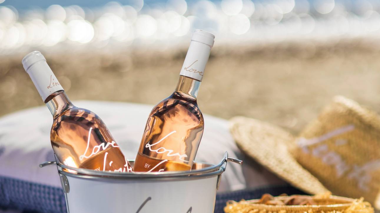 Bottles of sustainable wine by Chateau Leoube in a branded ice bucket on a beach in Provence
