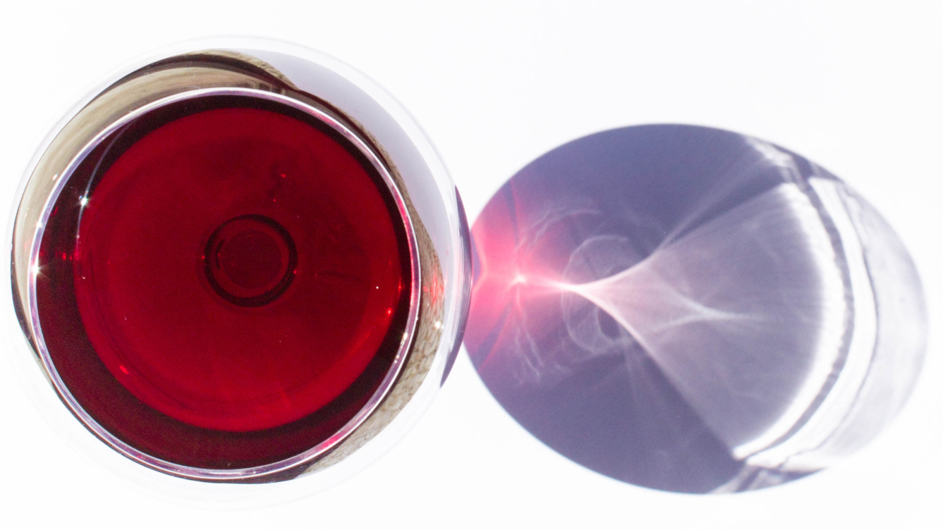 Glass of red wine over a white surface with light shining through the glass
