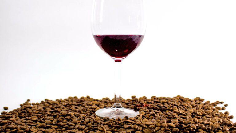 Glass of red wine surrounded by lots of coffee beans to represent wine and coffee similarities