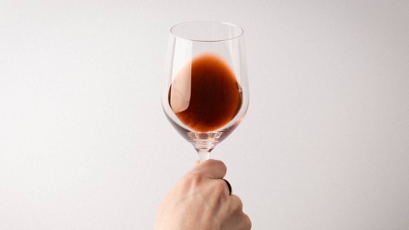 Person holding a glass of oxidised red wine over a white surface to show that it's got a brown hue