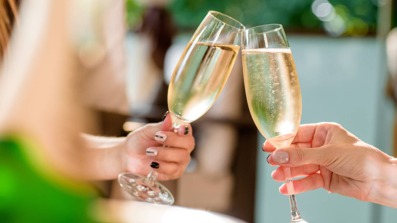 Two women toasting with flute glasses full of sparkling wine outside