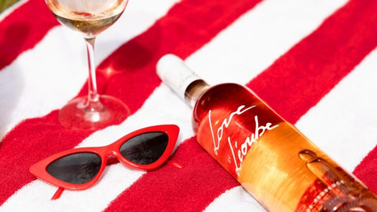 Bottle of Love by Léoube Organic Côtes de Provence laying on a red and white towel with red sunglasses to represent summer rose wine