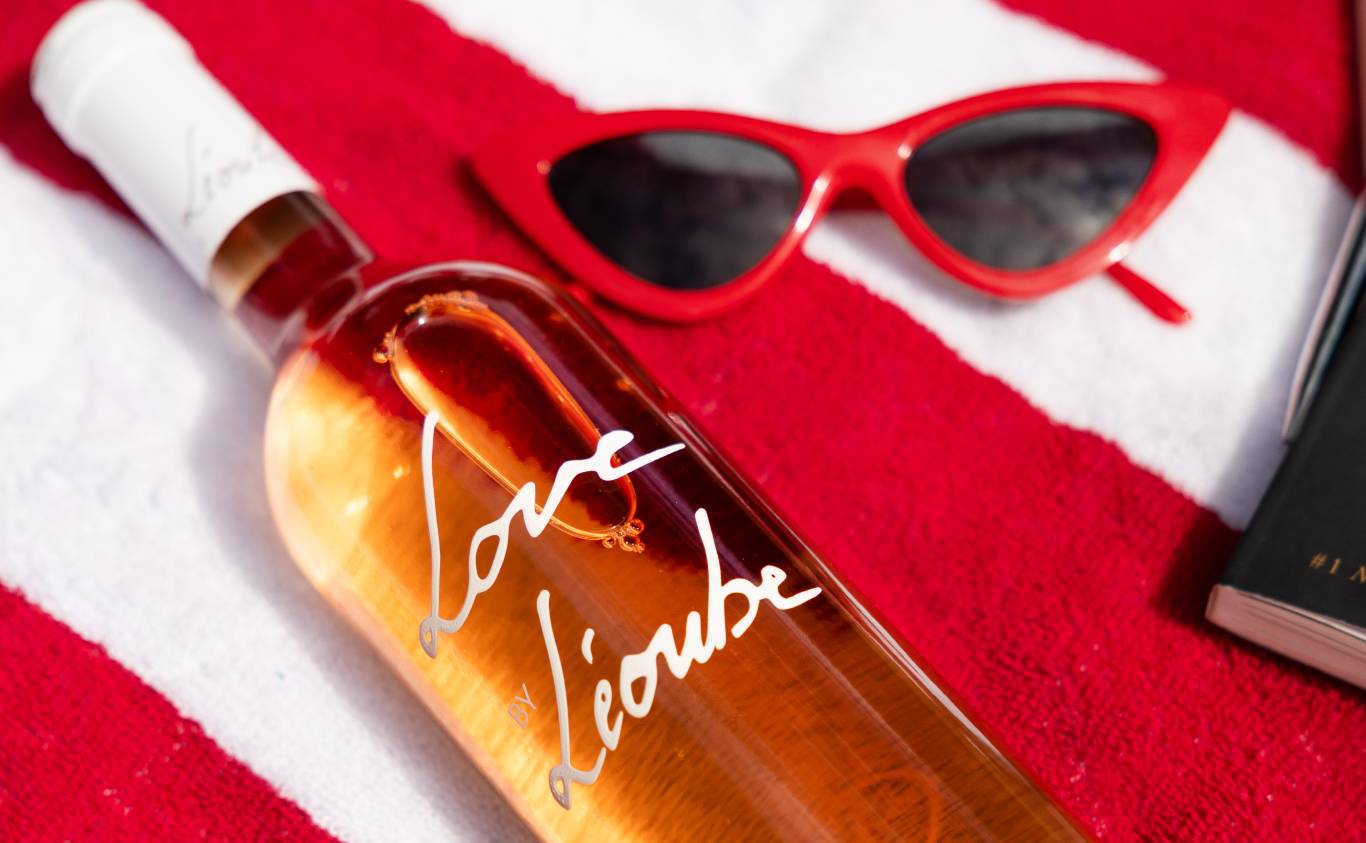 Bottle of Love by Léoube Organic Côtes de Provence laying on a red and white towel with red sunglasses and a book