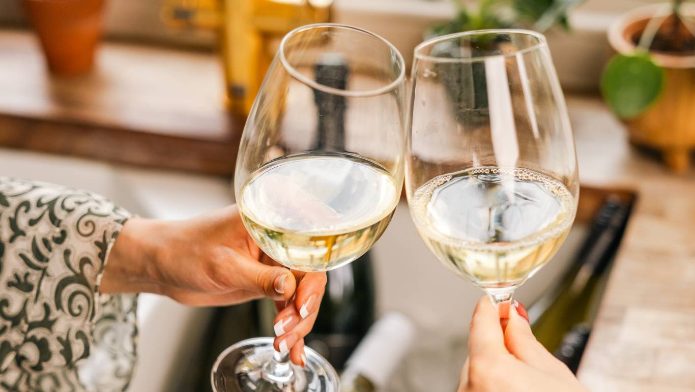 Two glasses of white wine being clinked by a kitchen sink