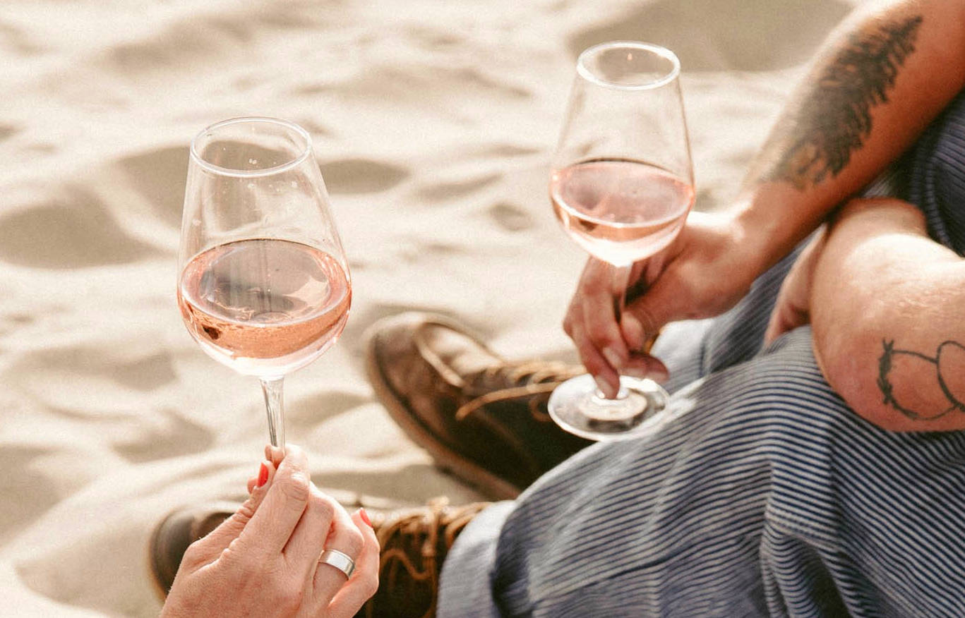 Two people drinking rose wine from Bordeaux on a sandy beach