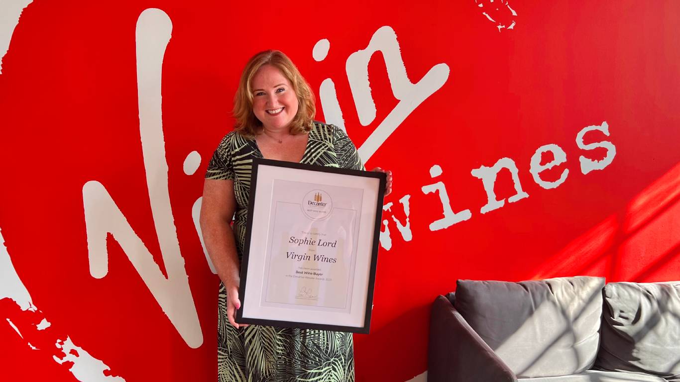 Head of Buying at Virgin Wines, Sophie Lord, holding up her Best Wine Buyer award from Decanter in front of a red Virgin Wines wall