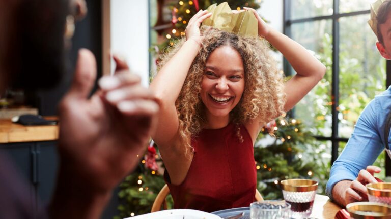 Happy woman wearing a Christmas cracker hat at the dinner table on Christmas Day to represent wines to pair with Christmas dinner