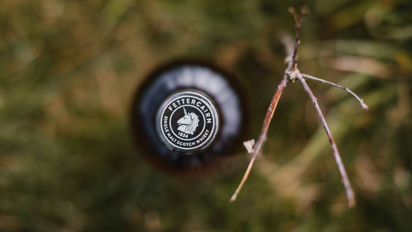 Looking down at a bottle of Fettercairn whisky outside with all the camera focus on the logo