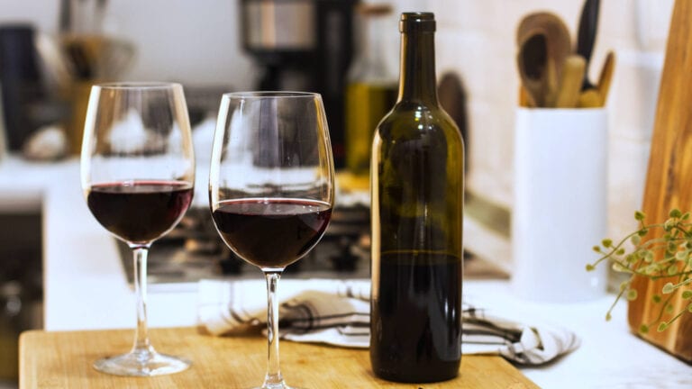 Open bottle of red wine in a kitchen beside 2 glasses of red wine