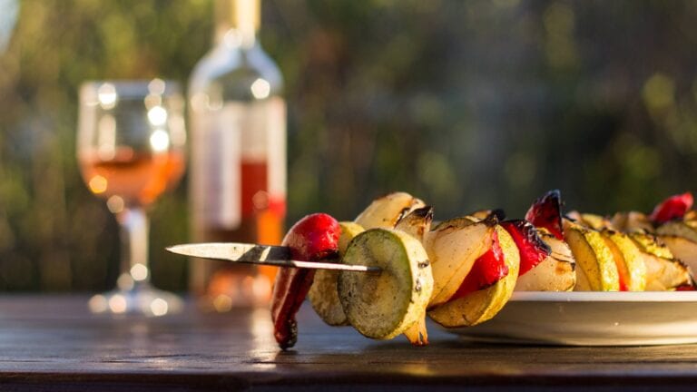 Glass and bottle of rose wine next to a BBQ skewer