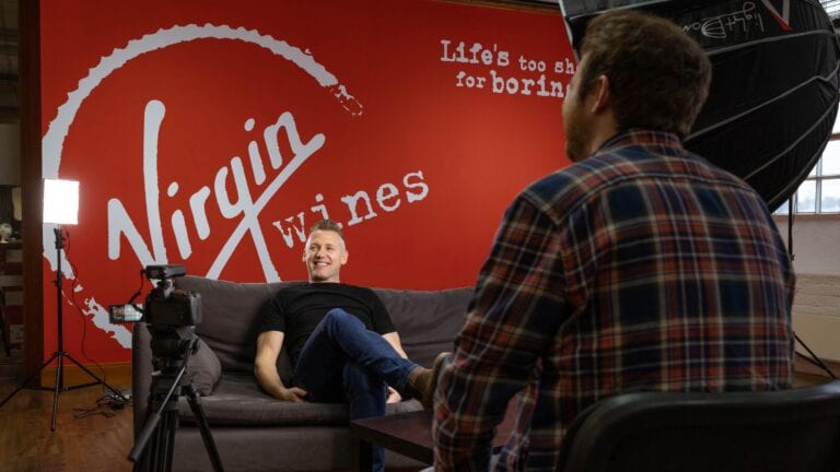 Wine Buyer at Virgin Wines, Andrew Baker, being interviewed in front of Virgin Wines branded wall